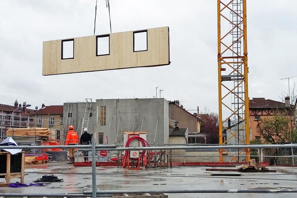 Les panneaux de façade sont approvisionnés par la route, manutentionnés avec la grue du chantier et assemblés à l’aide de tirefonds. [©Agence Viguier]