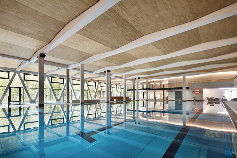 Le plafond qui ne fait pas de vagues et qui fait des vagues : pour cette piscine, le plafond Lignoakustik est posé en dent de scie grâce à la disposition des lisses en bois fixées sur les poutres en béton. [©Lignotrend]