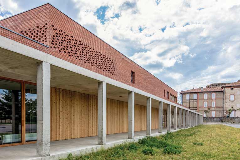 Vue de la façade intérieure du réfectoire, du préau et du parc de l’établissement. Au fond, le bâtiment existant. [©Cros & Leclercq Architectes]