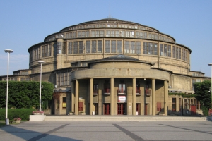 L'entrée principale de la Halle du Centenaire. Le dôme est couvert d'un toit en escalier flanqué d'une multitude de fenêtres, dont l'entourage est constitué d'un bois dur exotique. [©DR]