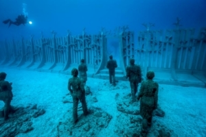 L’ensemble “Traverser le Rubicon” se compose d'un groupe de 35 personnages, qui marchent vers une entrée et un mur sous-marins. Ce dernier, qui est à la fois industriel et organique, s'étend de 30 m de long et 4 m de haut, et contient une seule porte en son centre. Il est la métaphore de l'absurdité, des notions de territoires, dans le monde naturel, qui plus est, sous-marin. [©Jason deCaires Taylor/CACT Lanzarote]