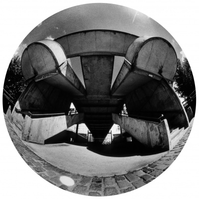 Qui reconnaît une partie de la Cité des Sciences et de l’Industrie, à La Villette, Paris XIXe ? Cette photo argentique avec un fisheye, donne un grain, un rendu et une perspective “extra-ordinaires”. Par sa lenteur de prise, ce procédé photographique aléatoire enlève tout mouvement à l’espace urbain, entraînant une confusion entre le passé et le futur. Ici s’élève une “Spider” (Araignée). ©Seka